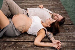 Eltern liegend mit Babybauch am See