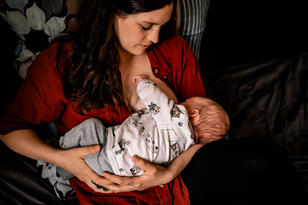 Fotobesuch im Wochenbett 3 Mama stillt Baby sitzend im Arm beim Wochenbettshooting