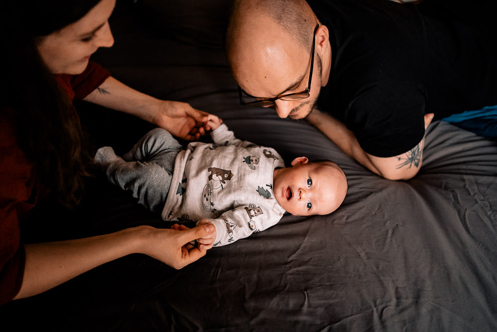 Fotobesuch im Wochenbett 1 Vater und Mutter bestaunen frisch geborenes Baby im Wochenbett zuhause