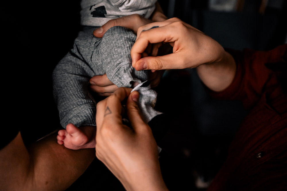 Fotobesuch im Wochenbett 9 zwei Hände ziehen dem neugeborenen Baby die graue Hose an