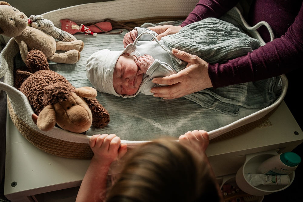 Schwester bestaunt kleinen Bruder im Wochenbett