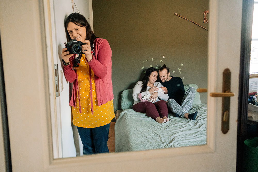 Fotografin im Spiegel wie sie Familie im Wochenbett im Bett fotografiert
