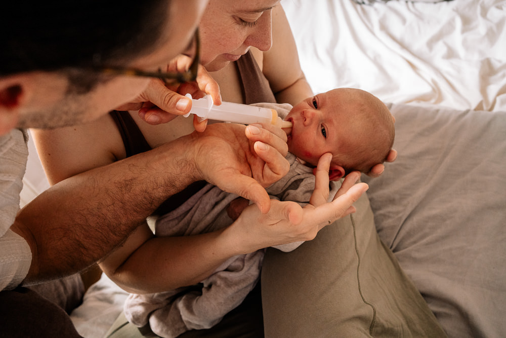 Eltern füttern Neugeborenem im Wochenbett bei Fotobesuch Wochenbettfotografin
